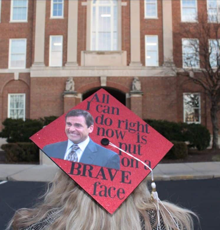 Red graduation cap with Michael Scott's face and the words all I can do right now is put on a brave face