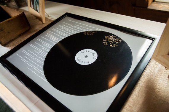 A framed vinyl record displayed as a guest book, with signatures and messages written in gold marker on the surface.