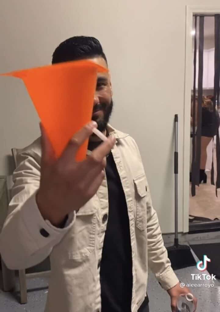 guy holding up orange traffic cone and cigarette