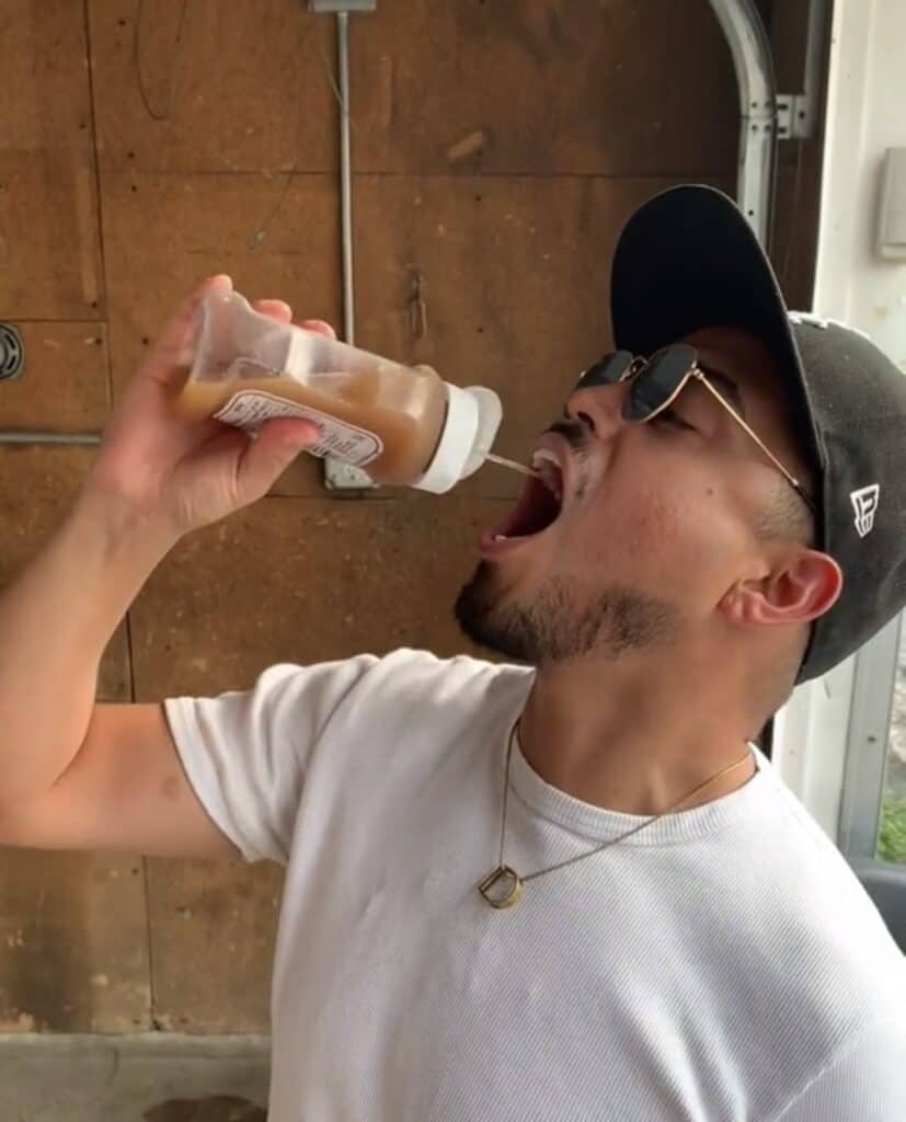 guy squirting brown liquid into his mouth from ketchup bottle