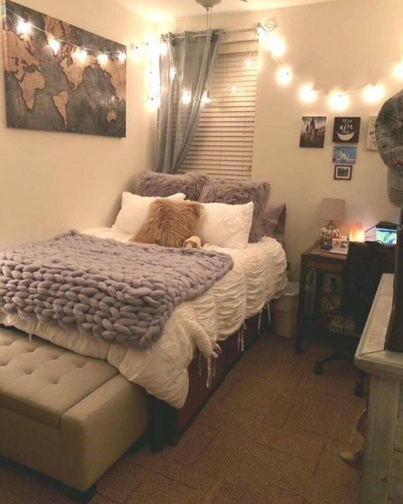 A warmly lit single dorm room with a textured white comforter and a chunky knit purple throw on the bed. A world map canvas and fairy lights adorn the wall.