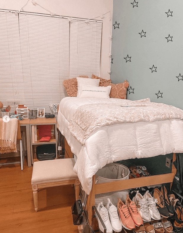 A colorful single dorm room with star wall decals, white linens and coral pillows on the bed, and a shoe rack.