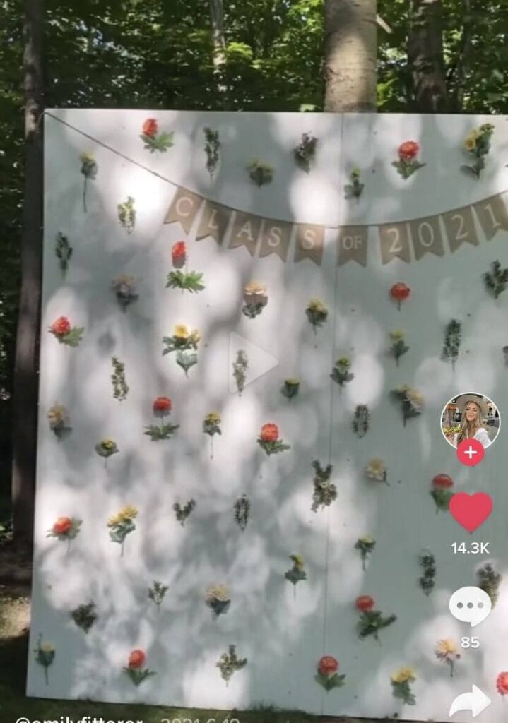 A white photo booth backdrop with stems of flowers attached to it at an outdoor graduation party