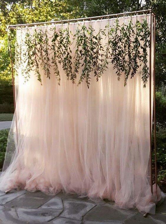 blush pink tulle photo backdrop with hanging greenery in an outdoor setting