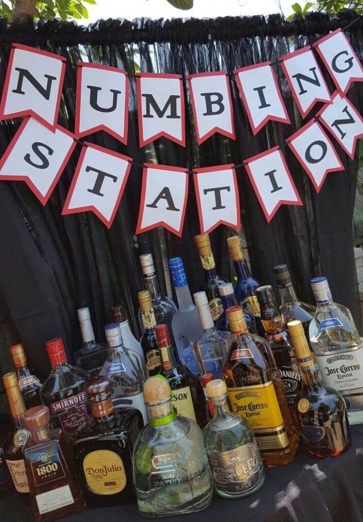 Bottles of alcohol set out on a graduation party table with a banner that says numbing station.
