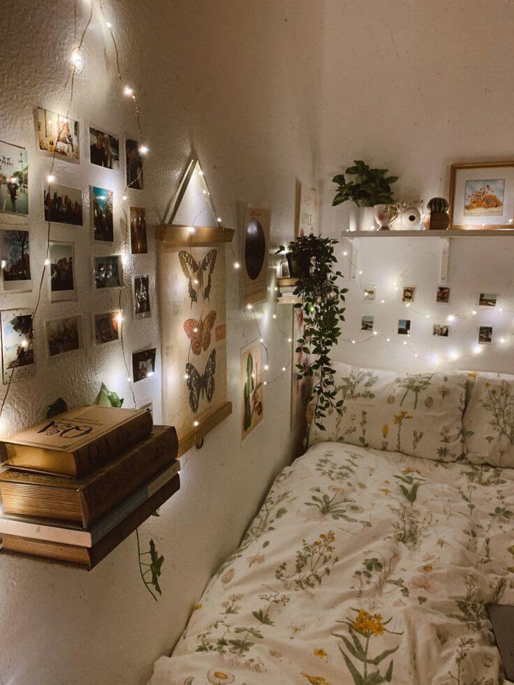 A cozy dorm room corner with a botanical theme. The bed is adorned with a floral-patterned comforter, and the walls are decorated with polaroid photos, string lights, and hanging greenery.