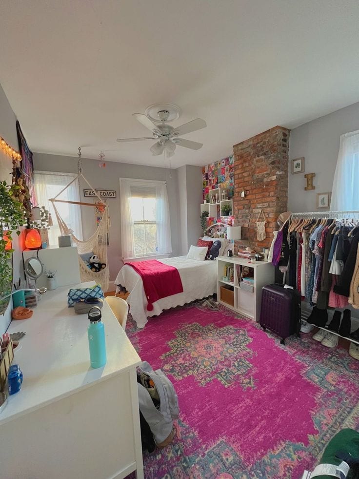 A bright and eclectic dorm room featuring a vibrant pink area rug with an intricate pattern.