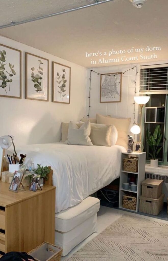 A minimalist decorated college dorm room featuring a bed with white linens, a desk adorned with personal pictures, and framed artwork on the wall. Underneath the bed is a storage ottoman.