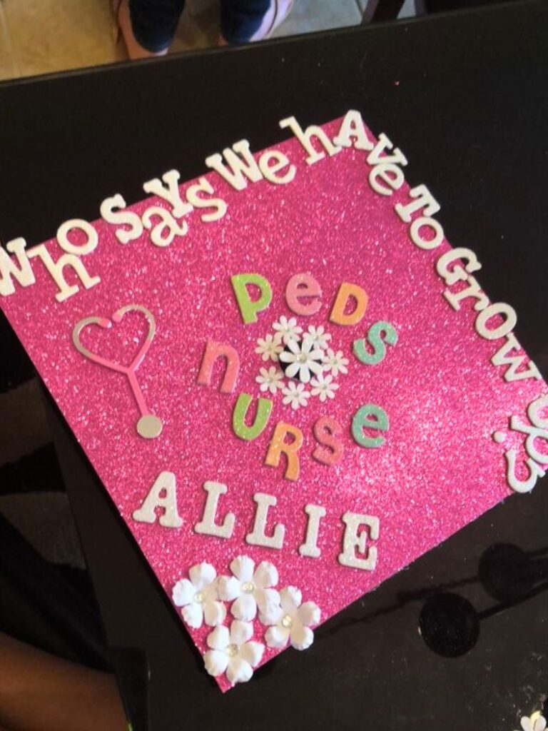 A glimmering pink graduation cap with the whimsical phrase 'who says we have to grow up' in white letters, followed by 'Peds NURSE ALLIE' featuring a stethoscope, heart, and colorful letters.